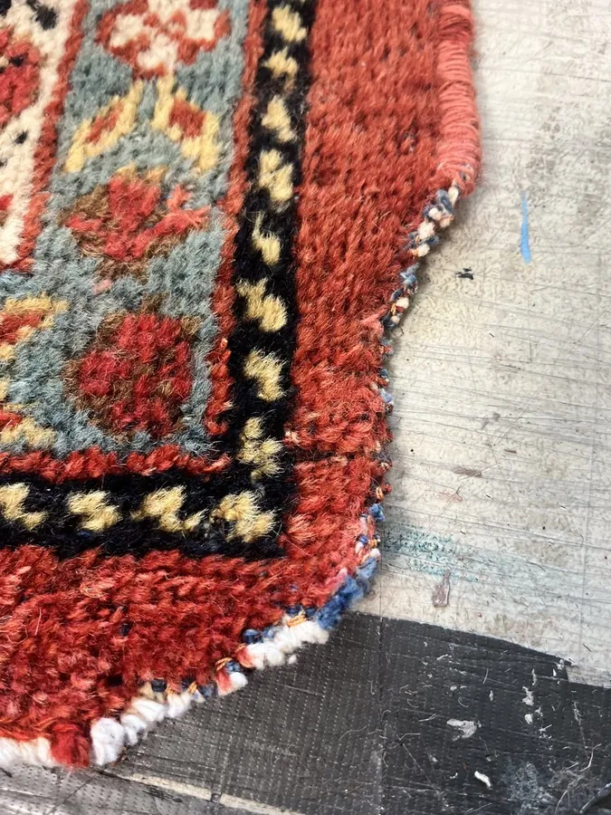 Red and teal Caucasian rug with damaged, unravelling corner